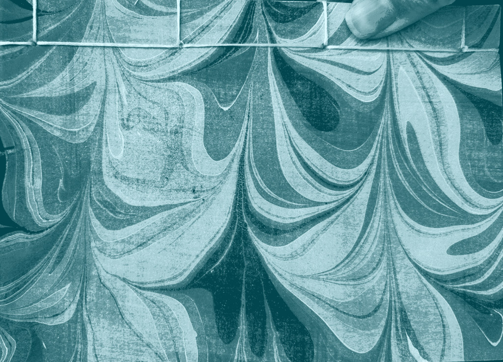 a thumb holds a japanese stab-bound book with a cover of marbled paper, the thumb holds the book from the spine, which is near the top of the image, and the book hangs down below, the marbling twirling towards the bottom of the page.