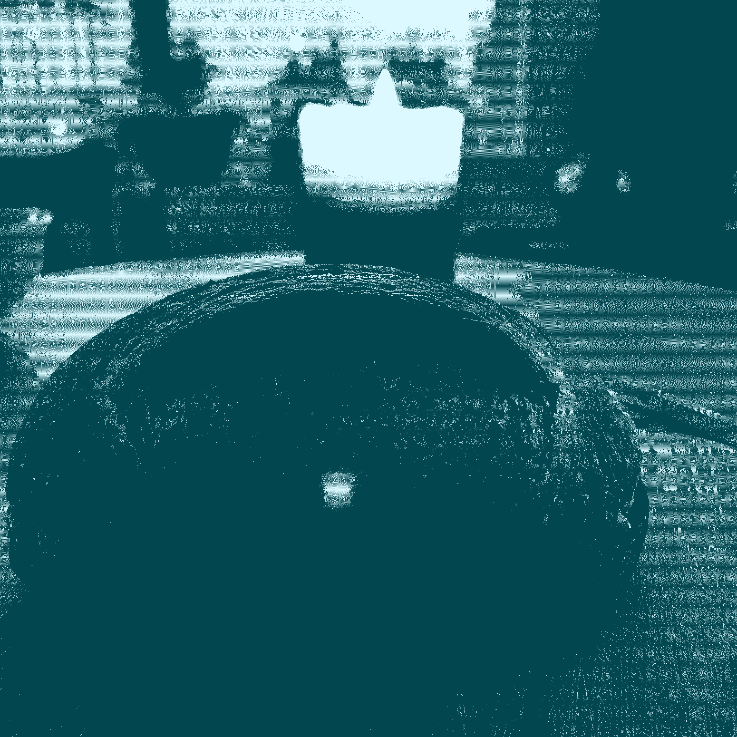 a loaf of sourdough bread rises in the foreground, and a beeswax candle burns behind it. behind the candle lies a building mid-construction, and blurry, out of focus. 