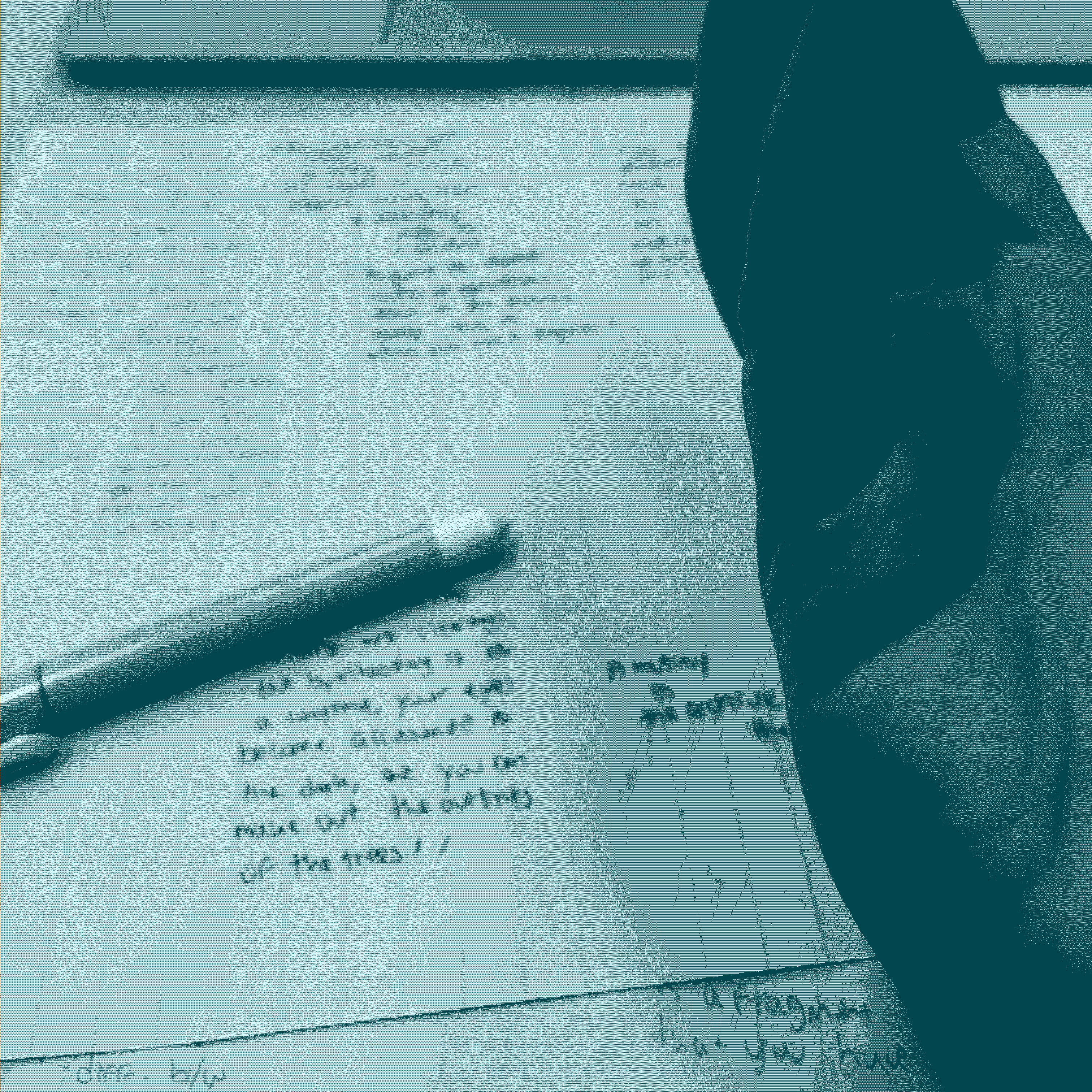 paper, ink, a pen, and a hand with ink stains dominate the foreground, the hand is titled towards the camera, and a shadow falls over the fingers.
